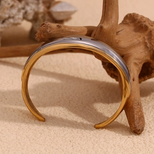 Detailed view of dual-tone 18K gold plated stainless steel open bangle on natural wood