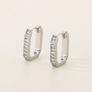 Macro shot of silver U-shaped earrings with inlaid rectangular zircons on a beige background