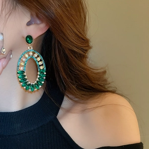 Close-up of vintage oval gold earrings with emerald green gems and sparkling crystals