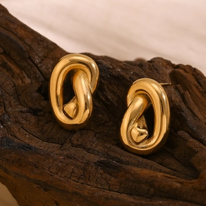 Macro shot of gold-plated knot stud earrings with heart detail on a wooden base
