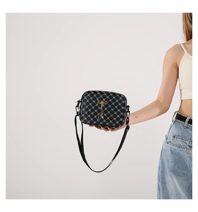Close-up of black monogram texture and metal pendant detail on a stylish crossbody bag