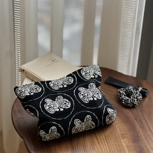 Détail de la trousse en toile noire avec broderie papillon blanche sur une table en bois
