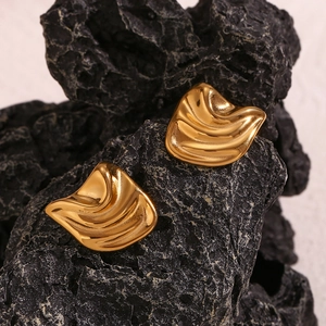 Close-up of gold irregular geometric wave studs on dark volcanic rock background