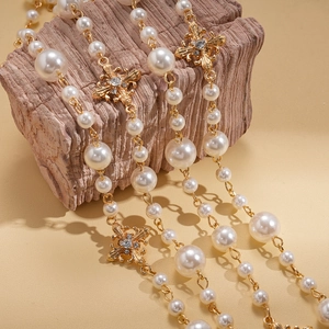 Détail du collier de perles avec breloques dorées florales et accents de cristal