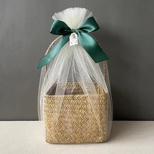 Detail of seagrass basket featuring white tulle wrap and a large dark green satin bow