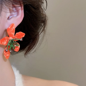 Detail view of bold orange flower earring with green bead center on model's ear
