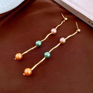 Detail of gold wavy fringe earrings featuring colorful pearls on dark silk background