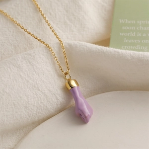 Detail shot of golden necklace featuring a purple fist pendant on white fabric background