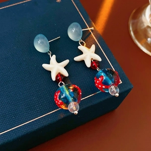 Detailed close-up of starfish earrings with red and blue glass beads on jewelry box
