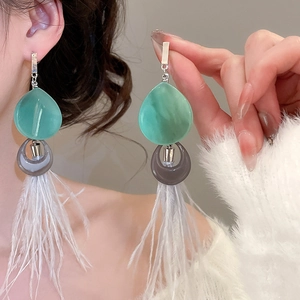 Détail de boucles d'oreilles bohèmes avec résine bleu sarcelle et plumes blanches