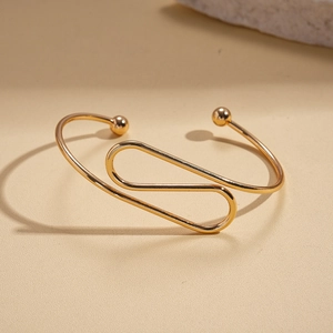 Detail of twisted gold metal cuff bracelet with round spheres on minimalist beige background