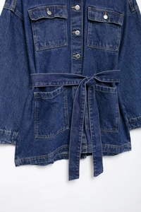 Close-up of deep blue denim jacket showing metal buttons and adjustable waist belt