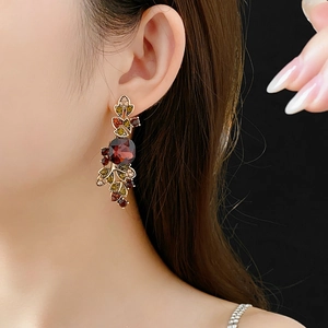 Close-up of vintage gold earrings with red oval gemstone and colorful leaf-shaped crystals