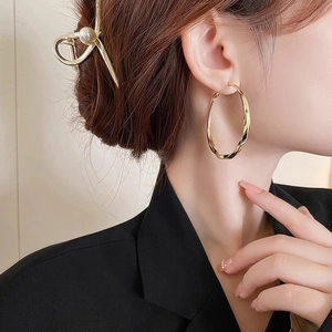 Close-up of a model wearing large golden twisted hoop earrings with a metallic finish
