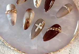 Detailed view of coffee-toned press-on nails with golden crosses and rhinestone accents