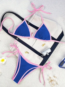 Detail of royal blue bikini with pink trim, flat lay on sand with beach accessories