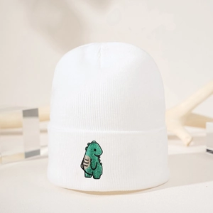 Detaillierte Nahaufnahme einer weißen Strickmütze mit grüner Cartoon-Dino-Stickerei