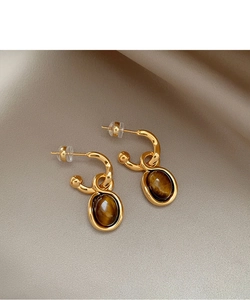Detailed macro of gold-plated tiger eye stud earrings on elegant champagne silk fabric