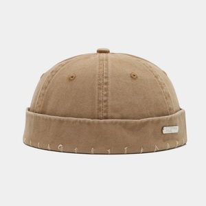 Détail du bonnet docker en coton kaki avec trous usés et plaque de logo en métal argenté