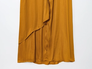 Detail of a ginger satin midi dress showing the irregular cut hemline on white background
