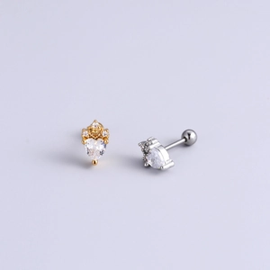 Close-up of heart-shaped zircon earrings with gold and silver barbell piercing studs