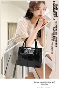 Glossy black crocodile pattern handbag with gold hardware displayed on white stairs