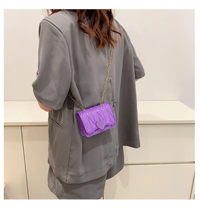 Detail of purple quilted mini crossbody bag with heart ornament and gold chain strap
