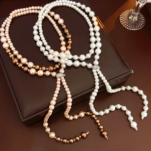 Detail of white and gradient faux pearl long necklaces with diamond clasps on a leather box