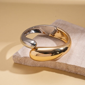 Macro shot of minimalist gold and silver intertwined open cuff on textured stone