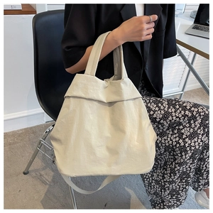Close-up of lightweight off-white nylon tote bag showing folding top and reinforced handles