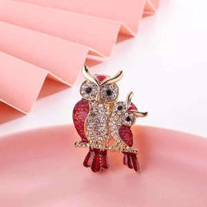 Macro shot of owl brooch with white crystals and red enamel on a golden branch
