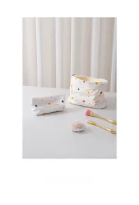 Close-up of two white cotton makeup bags with colorful dot patterns and top zippers