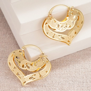 Detailed macro shot of golden heart-shaped hollow earrings with floral filigree patterns