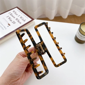 Hand holding a tortoiseshell pattern hollow square claw clip with gold metal spring