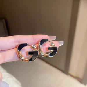 Detailed close-up of geometric black and gold letter G earrings with crystal accents