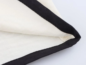 Close-up of white crepe fabric with contrast black trim detailing and high-quality stitching