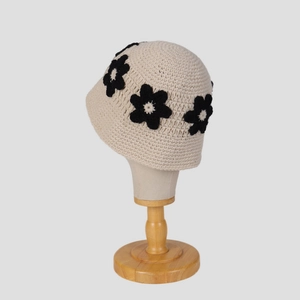 Détail d'un chapeau cloche beige crocheté main avec fleurs noires sur un support en bois