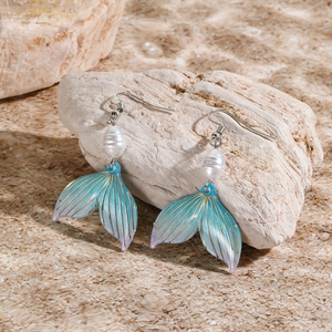 Macro detail of ocean-style fishtail earrings with blue gradient and white pearl accents
