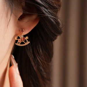 Detailed view of rocking horse earrings with gold plating and cubic zirconia on ear