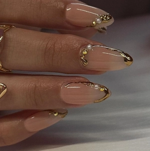 Faux ongles style français avec base nude, lignes dorées, perles et strass brillants