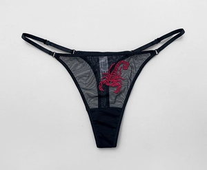 Detail of sheer black mesh thong featuring intricate red scorpion embroidery and straps