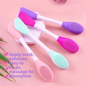 Double-headed silicone face mask brushes in four colors on a white geometric platform