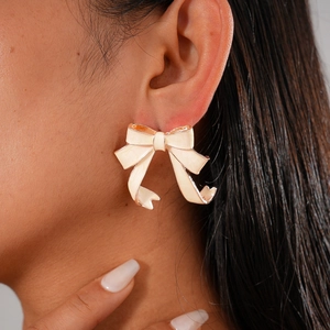 Close-up of retro cream enamel bow earrings with gold metal edges worn on model