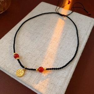 Close-up of golden Fu character pendant on black woven cord with red beads in warm light