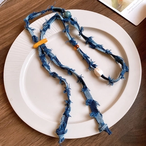 Dettaglio collana denim vintage con perline arancioni e ciondolo in ceramica floreale