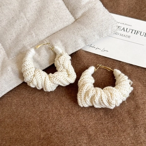 Vue détaillée des créoles tricotées beige avec fermoir doré sur tissu texturé doux