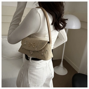 Détail du sac bandoulière en paille avec broderies florales et boucle nœud doré