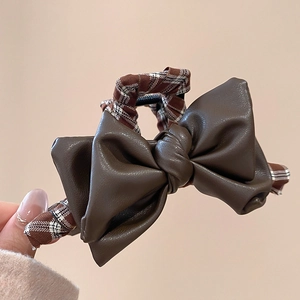 Detailed view of elegant brown leather bow hair clip with vintage plaid fabric details