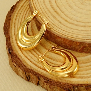 Polished gold U-shaped horseshoe earrings with textured grooves on a wooden stand