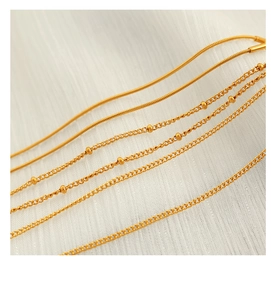 Vue détaillée de chaînes en or de types serpent et perles sur tissu blanc pur